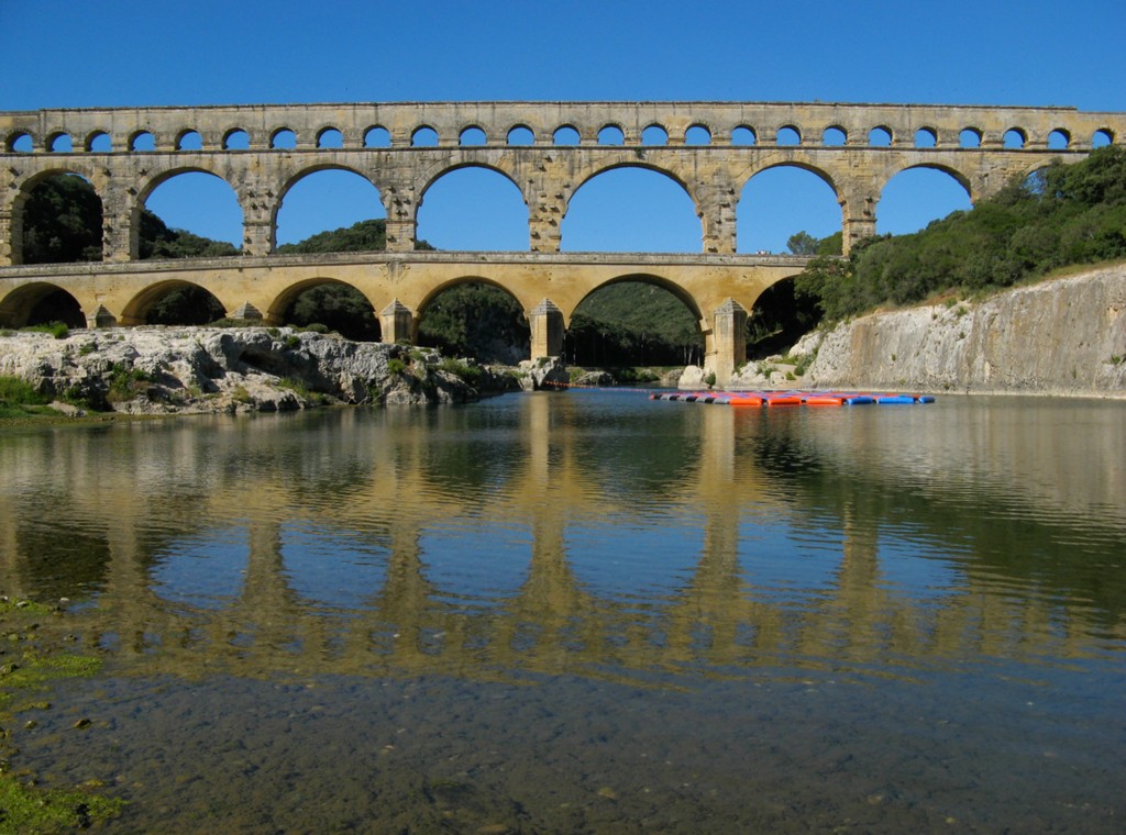 Pont du Gard visto desde el río, con tres niveles de arcos. Sobre la hilera de arcos pequeños se encuentra el recorrido de la conducción.